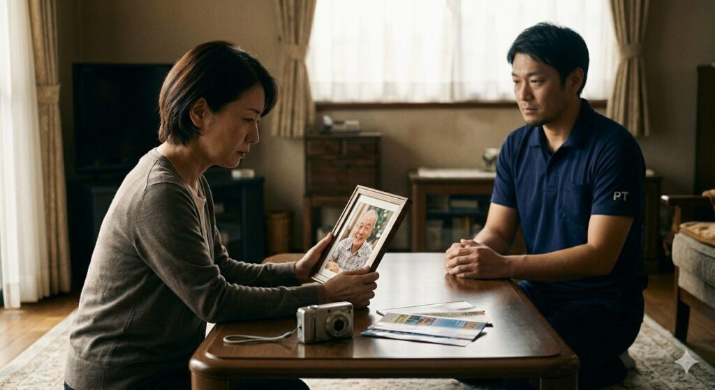 静かなリビングで、亡くなった父の満面の笑顔の遺影を抱えて涙を流す女性と、その傍らで静かに見守る理学療法士。先延ばしにした後悔を象徴する場面。